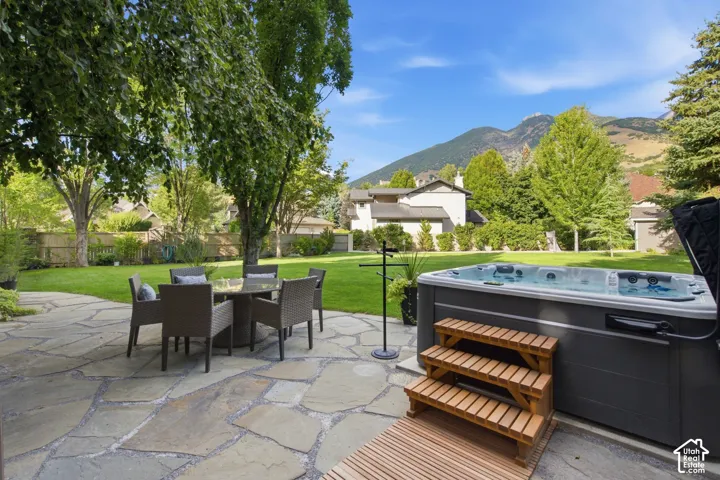 Expansive backyard featuring a natural stone patio, a hot tub with wooden steps, and a lush green lawn