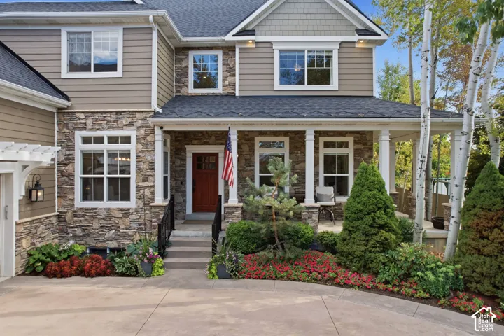 Stone and siding exterior with a covered porch, wood entry door, and manicured landscaping