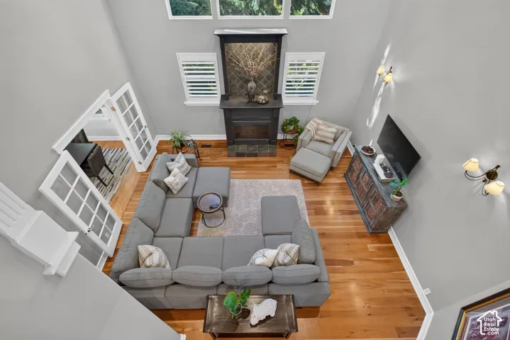 High vaulted ceiling with upper windows, wood-finish flooring, a fireplace featuring a dark mantel and tile surround, and French doors