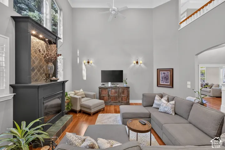 Soaring ceilings featuring a ceiling fan, a fireplace with a tile surround and wood mantel, wood-finish flooring, and a second-story open railing