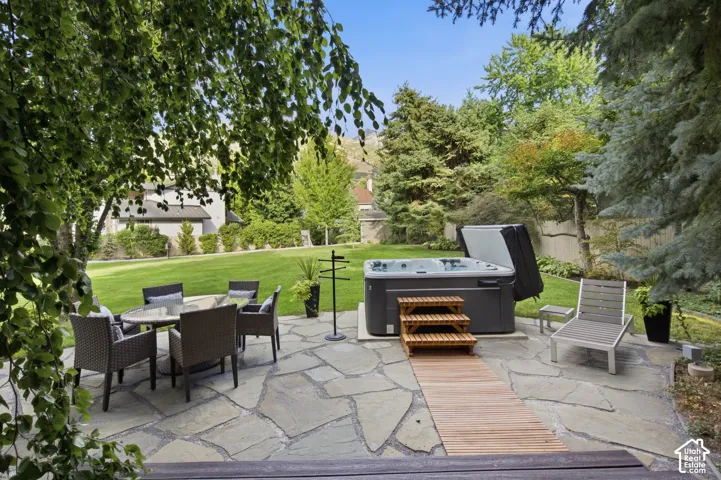 Expansive flagstone patio with a built-in hot tub, complemented by a large manicured lawn and mature trees