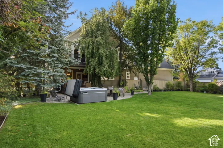 Expansive green lawn with mature trees, a stone patio, and a deck with a black metal railing