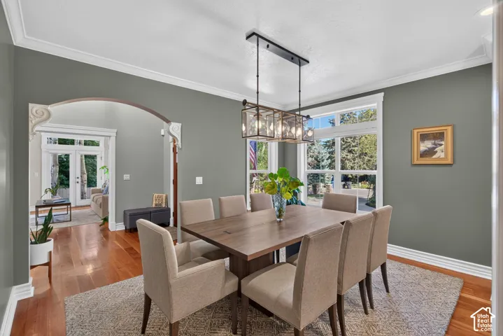 Hardwood flooring, arched doorway with decorative corbels, white crown molding, large multi-pane windows, and a rectangular chandelier with clear glass panels
