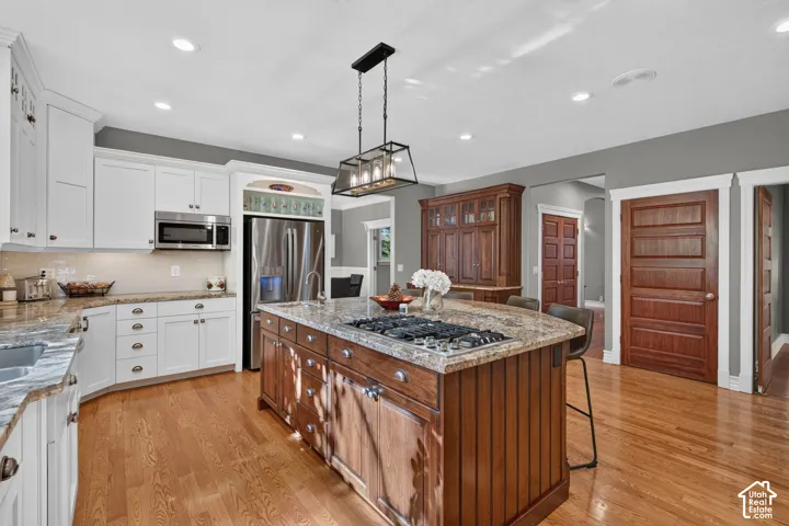 Open-concept kitchen featuring wood-finish flooring, white cabinetry, stainless steel appliances, and a central island with a built-in cooktop and stone-finish countertop