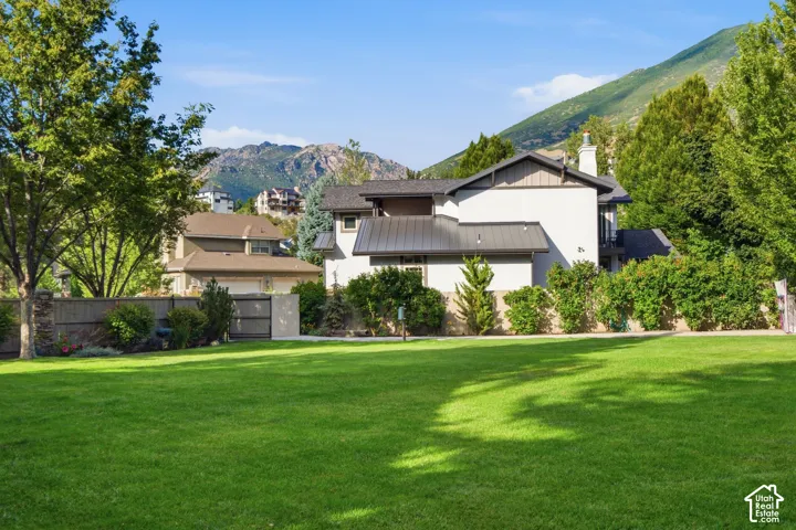 Expansive green lawn, mature trees, mountain backdrop, and stucco exterior with a metal roof
