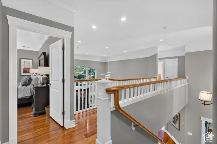 Hardwood flooring, white crown molding, recessed lighting, white paneled doors, and a wood and white banister