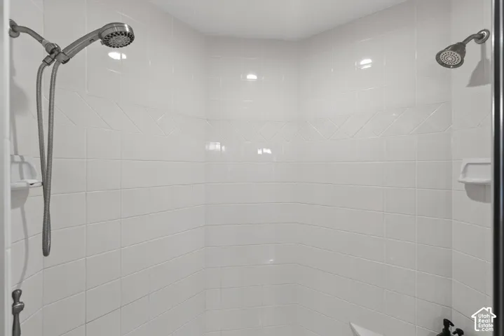 Shower enclosure featuring white ceramic tile walls, decorative accent tile band, fixed shower head, and an additional handheld shower fixture