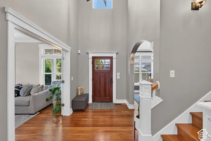 High ceilings, wood-finish flooring, solid wood entry door with glass panels, white trim, and a staircase with wood treads and white risers