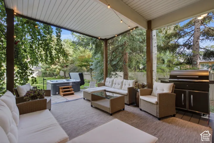 Covered patio with string lighting, a built-in grill, a hot tub, and a spacious outdoor rug