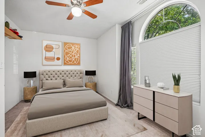 Arched window with honeycomb blinds, ceiling fan with integrated lighting, wall-mounted shelving, and carpeted flooring