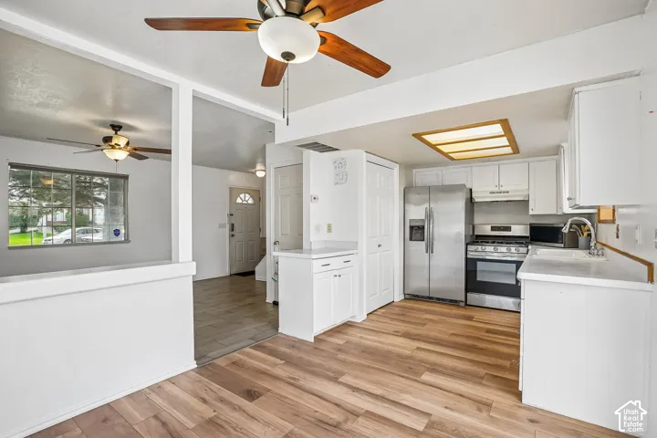 Wood-finish flooring, white cabinetry, stainless steel appliances, and a ceiling fan with integrated lighting