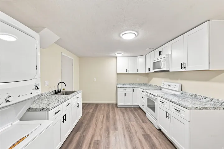 Full kitchen featuring white cabinetry with black hardware, stone-finish countertops, and wood-finish flooring