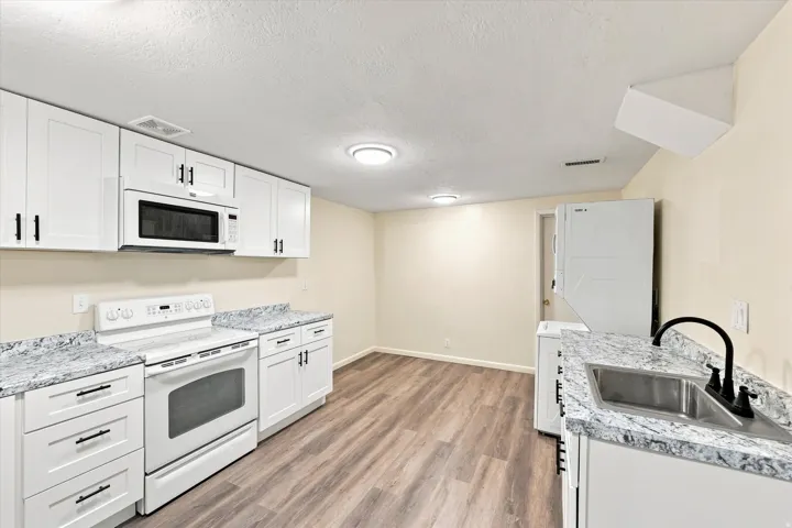 Updated kitchen featuring white shaker cabinetry, granite-style countertops, a stainless steel sink with a matte black faucet, and wood-finish flooring