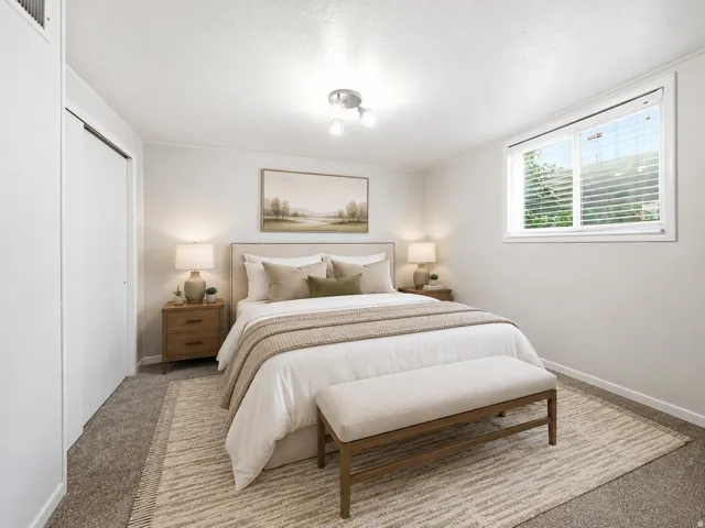 Basement bedroom with recessed window with blinds, overhead light fixture, light gray wall paint,