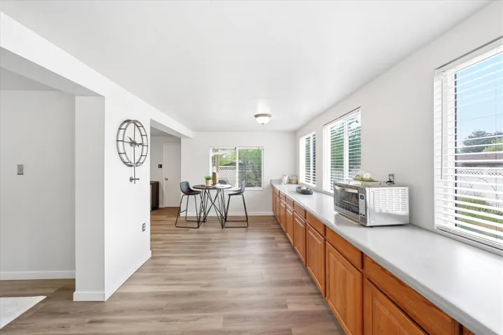 Wood-finish flooring, white walls, multiple windows with blinds, built-in lower cabinetry, and a long countertop