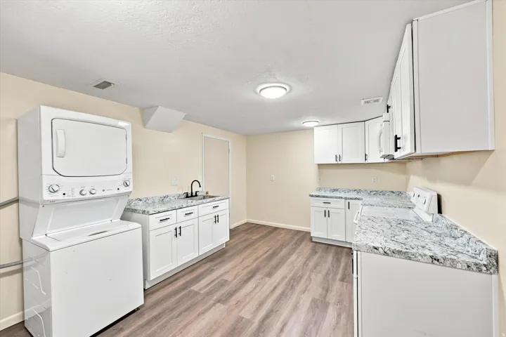 Wood-finish flooring, white cabinetry, integrated sink, granite-pattern countertops, and a stackable washer/dryer