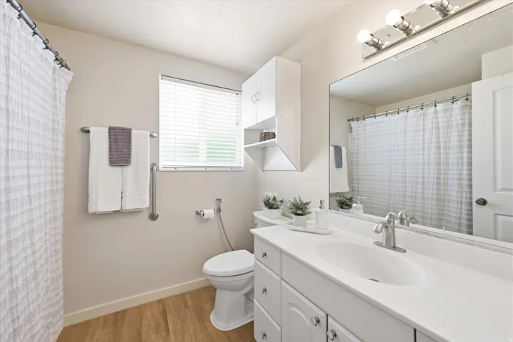 Main floor white vanity with integrated sink, brushed nickel faucet, large wall-mounted mirror, and wood-finish flooring