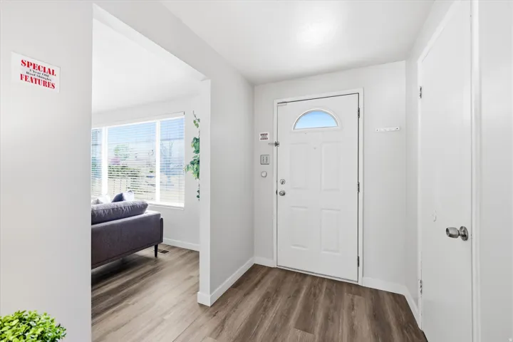 Bright entryway showcasing a white six-panel entry door with transom window, wood-finish flooring throughout, and clean white walls with recessed lighting