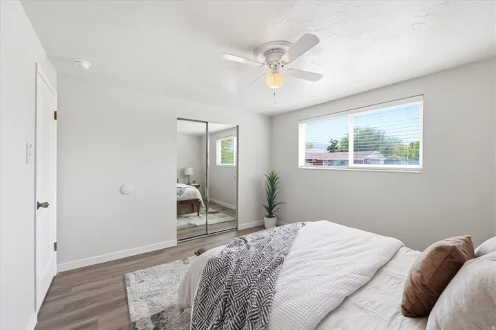 Large main floor bedroom with wood-finish flooring, white baseboards and ceiling fan.