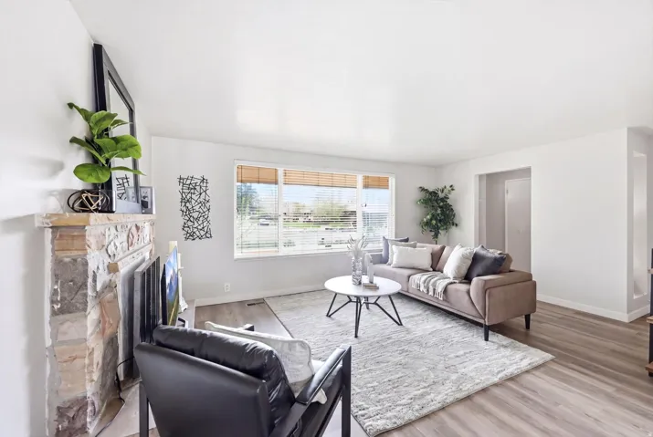 Spacious living area featuring a stone fireplace, wood-finish flooring, and a large window with blinds