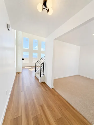 Wood-finish flooring, staircase with metal railings, high ceilings, multiple window arrangement, and recessed lighting