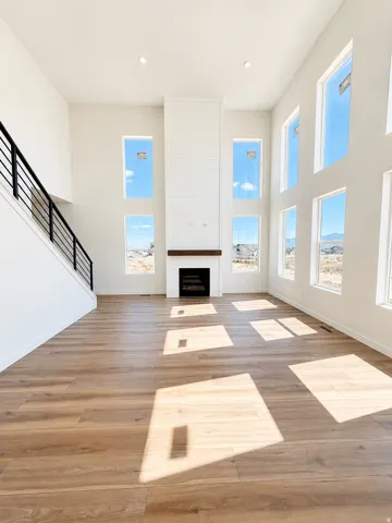 Two-story ceiling, multiple tall windows, modern fireplace with shiplap surround, wood-finish flooring, and a contemporary black metal stair railing