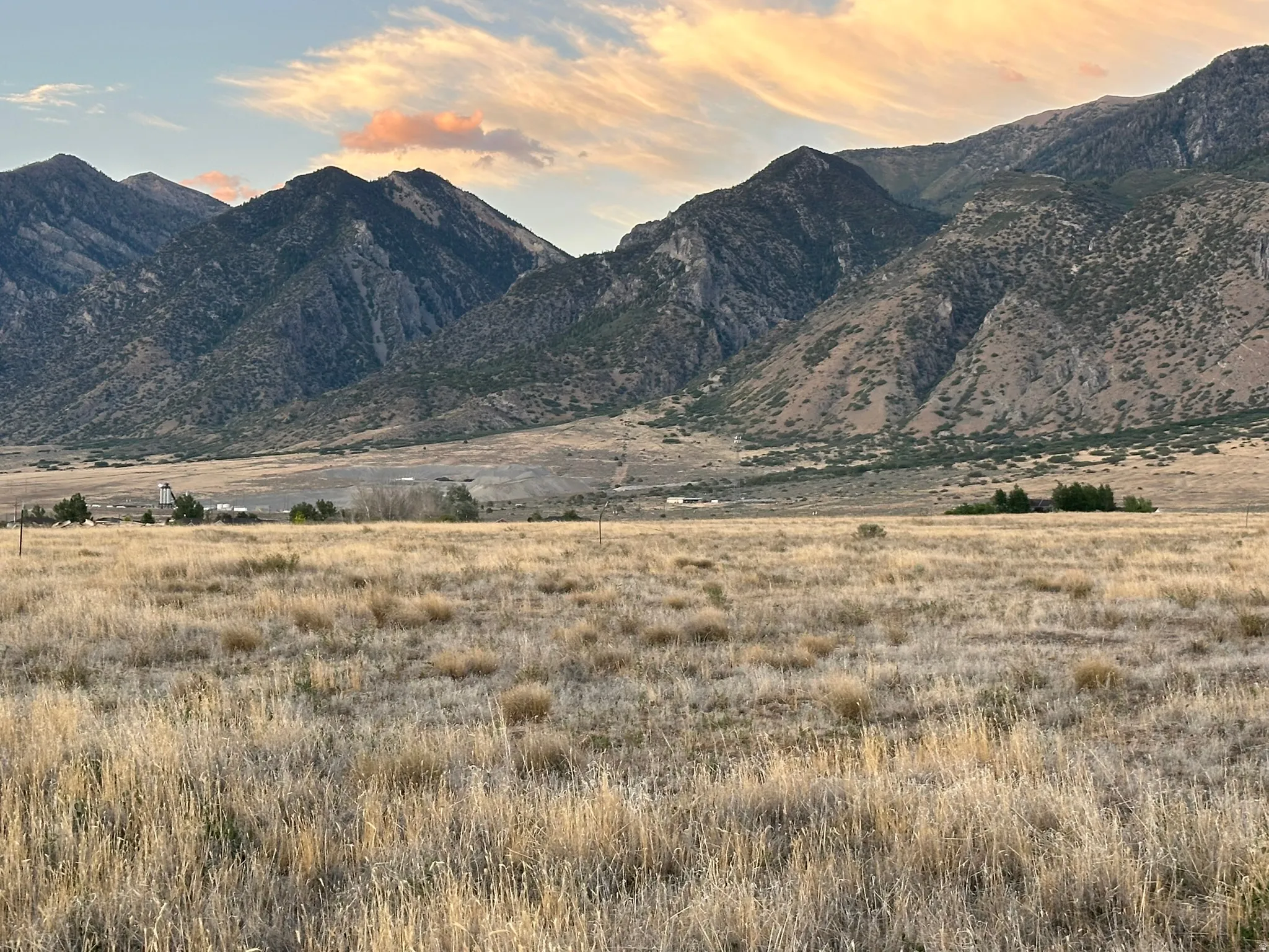 Expansive open land with natural grasses, featuring a mountain backdrop and distant structures