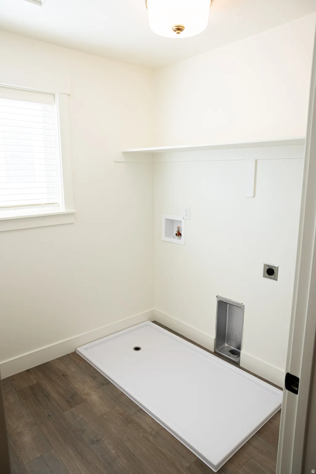 Laundry area featuring wood-finish flooring, white walls, overhead lighting, a window with blinds, and built-in shelving
