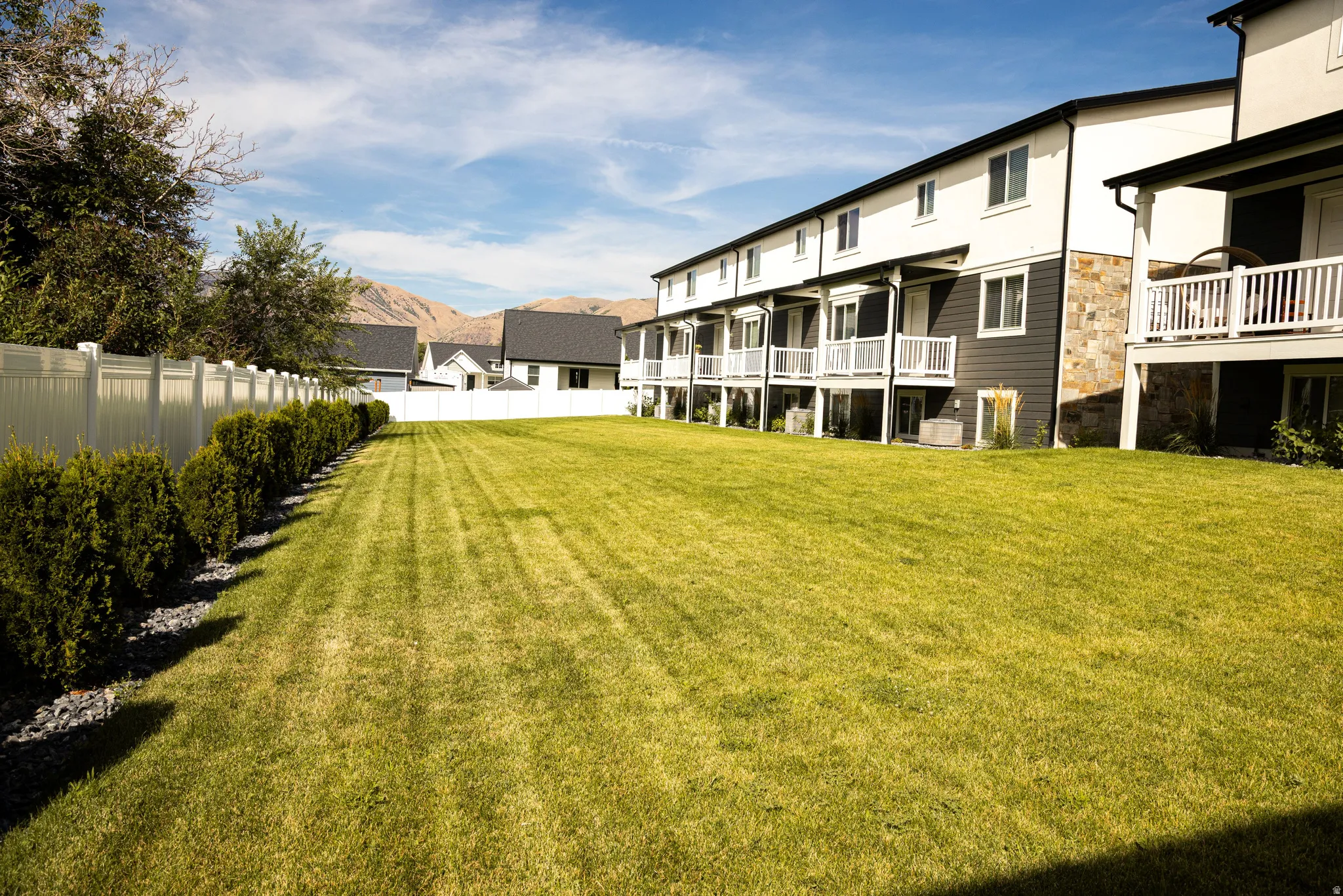 Expansive green space bordered by a white vinyl fence and mature shrubs
