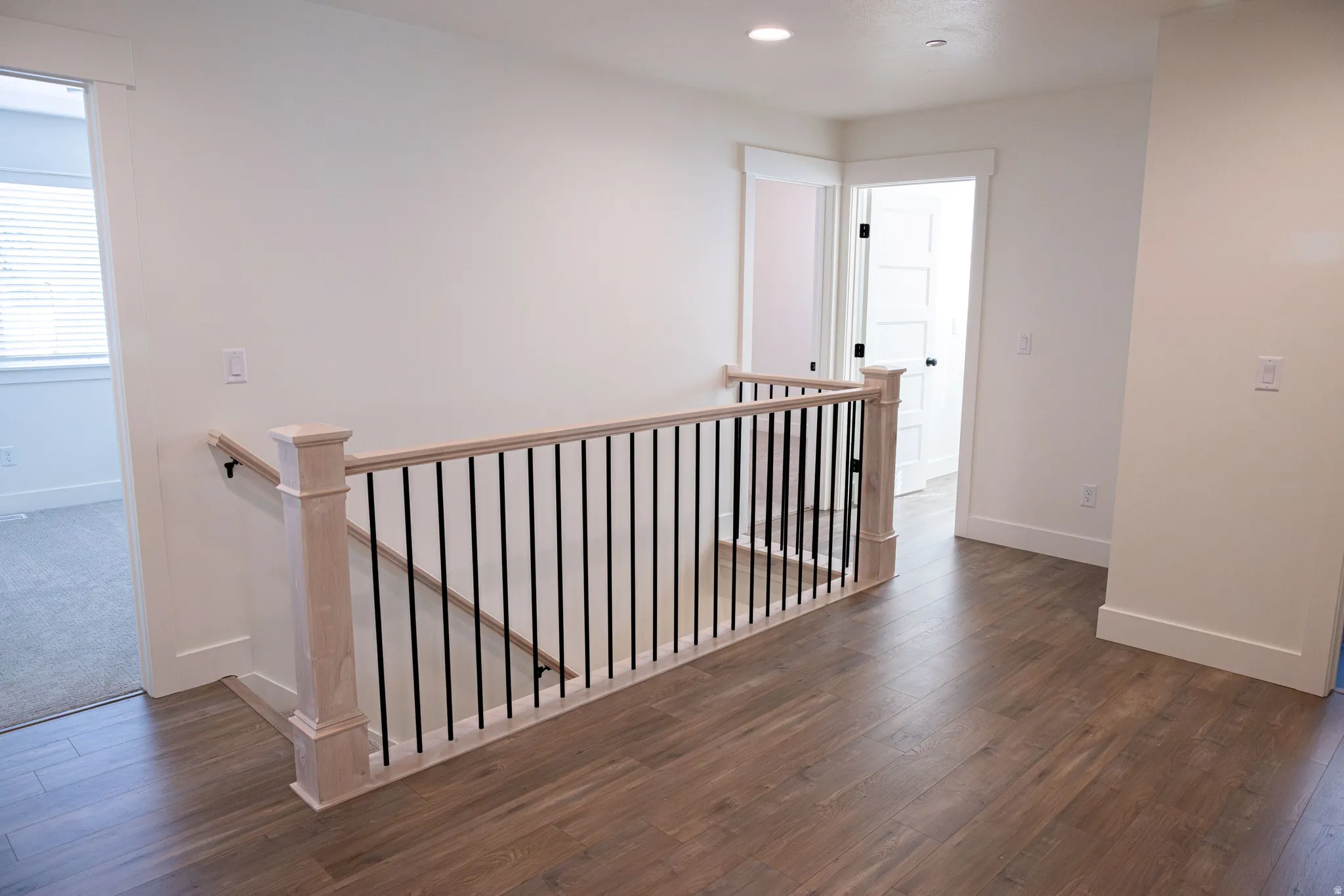 Wood-finish flooring throughout the landing and hallway, featuring a light wood newel post and handrail with black iron balusters