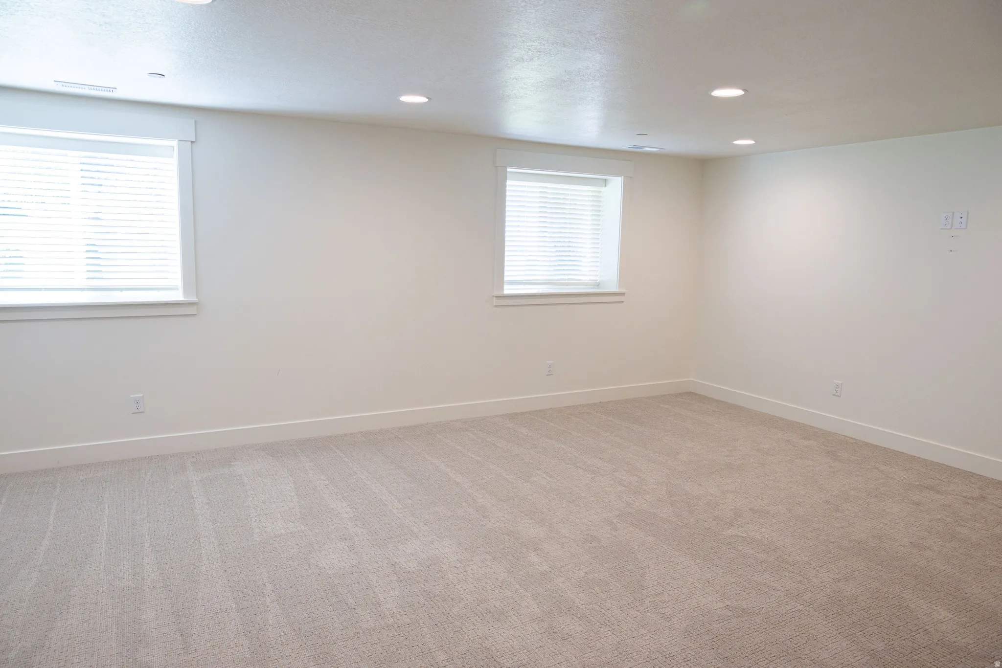 Bright room with recessed lighting, two windows with blinds, and light-toned carpeting