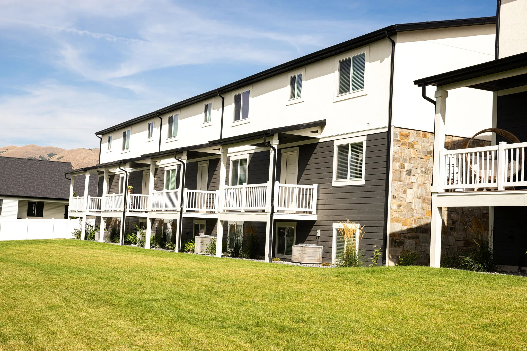 Contemporary townhome exterior featuring white siding, dark horizontal paneling, and stone accents