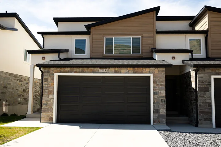 Contemporary exterior with a dark garage door, stone and horizontal siding accents, white trim windows, and a concrete driveway