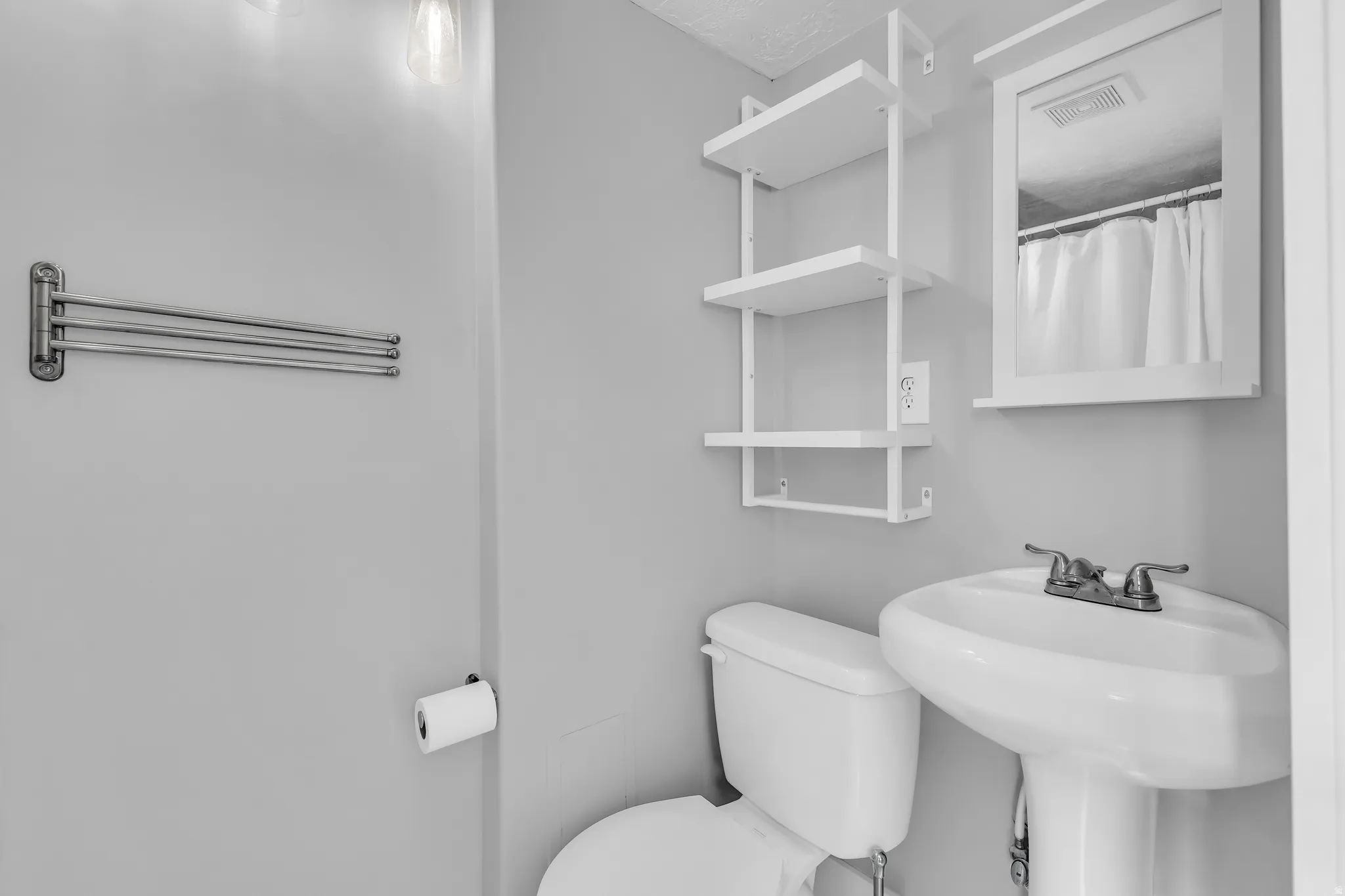 Pedestal sink with dual-handle faucet, wall-mounted mirror, built-in shelving, and white toilet