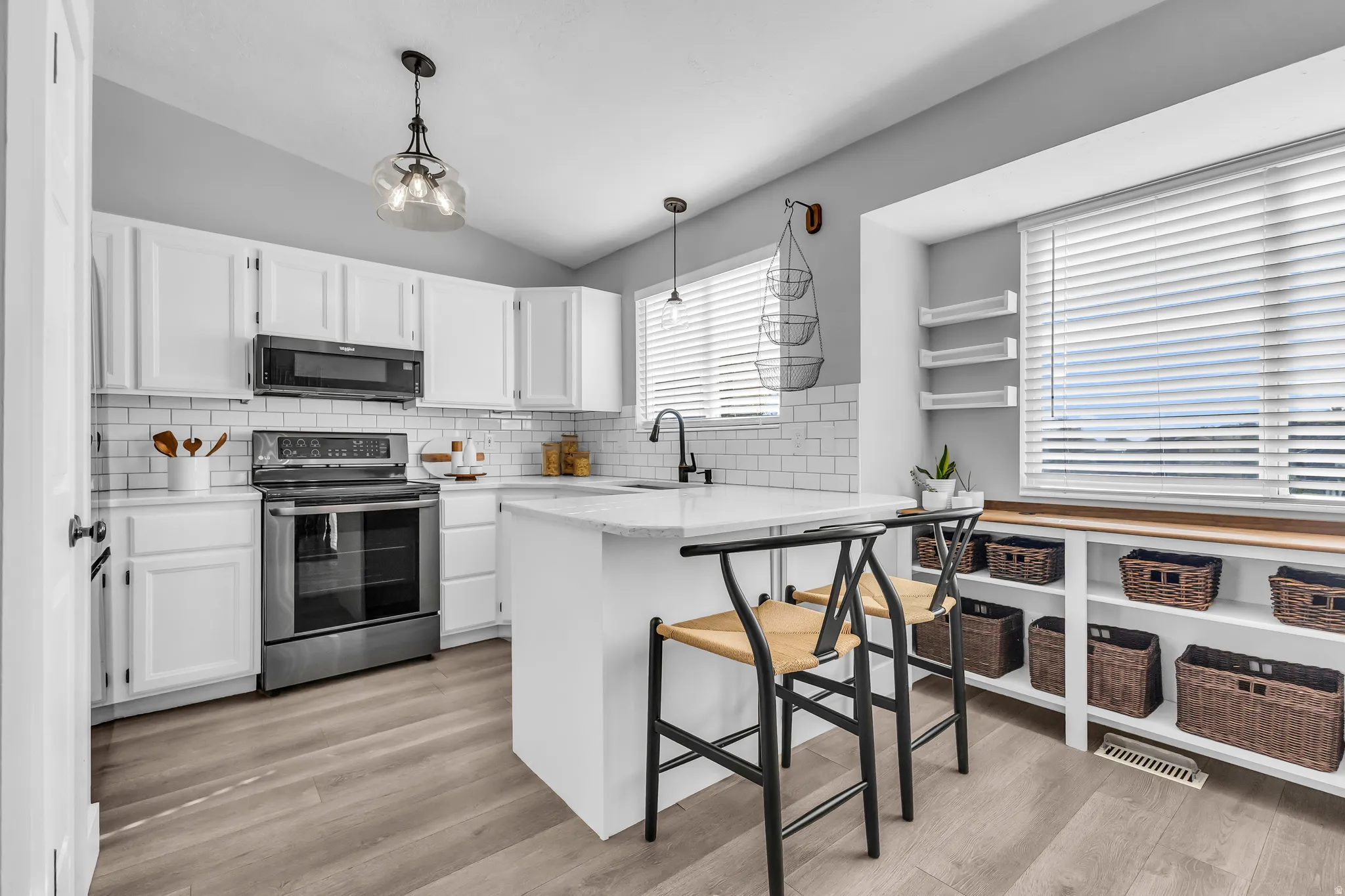 White cabinetry with dark hardware, subway tile backsplash, stainless steel appliances, large kitchen island with counter seating, and built-in shelving with wood-finish top