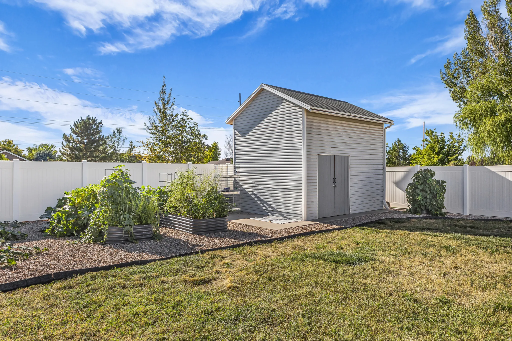 Backyard featuring a detached shed with double doors, white vinyl fencing, a gravel bed, and raised garden beds