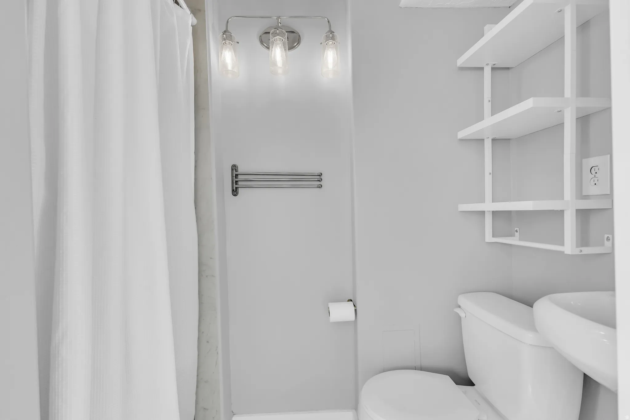 Three-light vanity fixture, white wall-mounted shelving unit, and white toilet