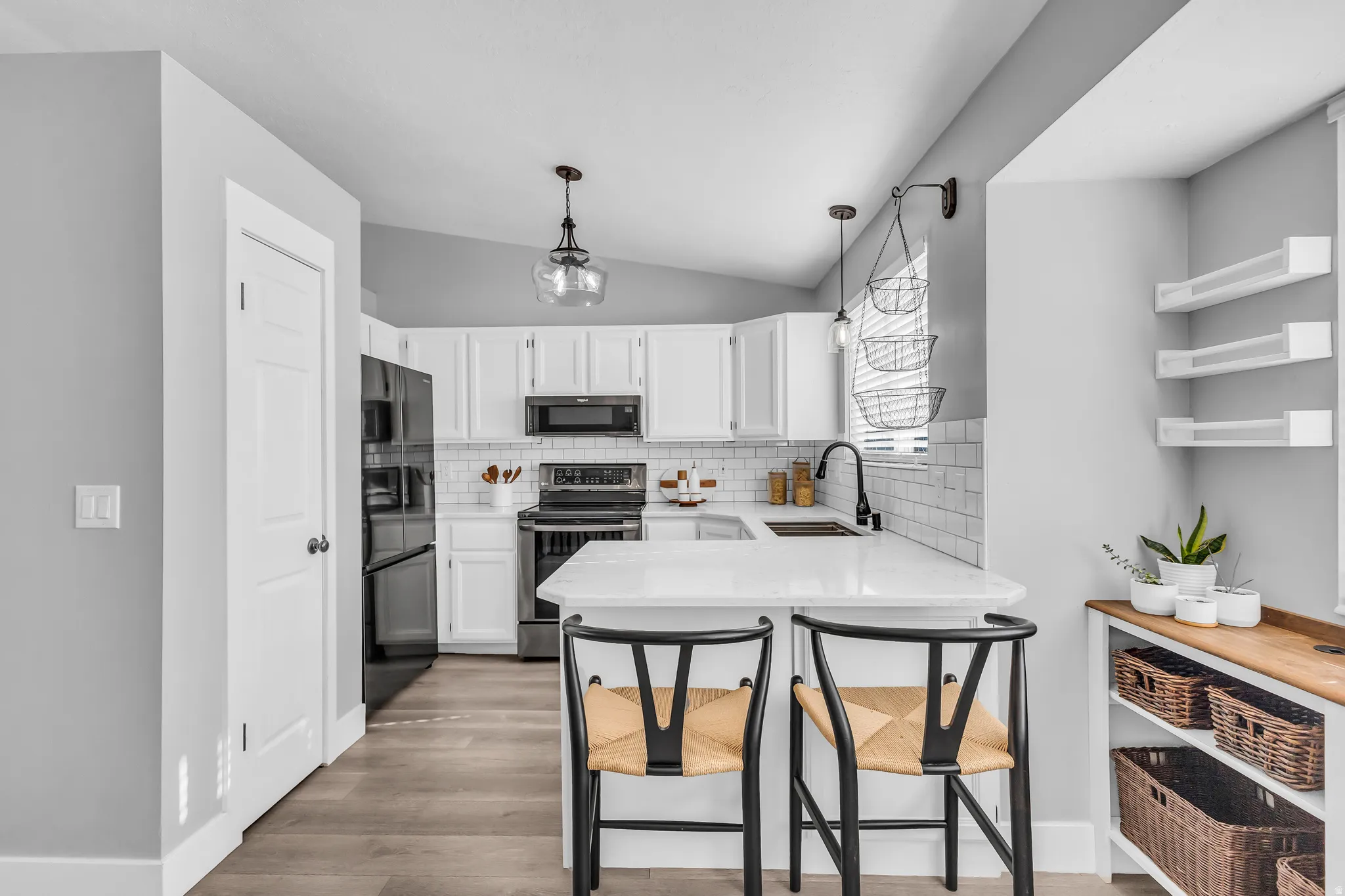 White cabinetry, black appliances, subway tile backsplash, wood-finish flooring, and a stone countertop peninsula