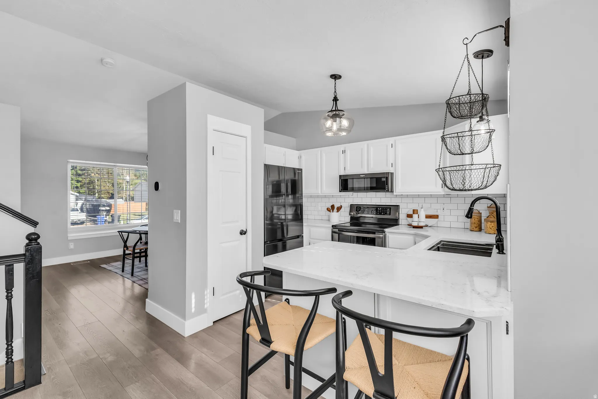Well-appointed kitchen featuring white cabinetry, light-toned countertops, subway tile backsplash, and black appliances