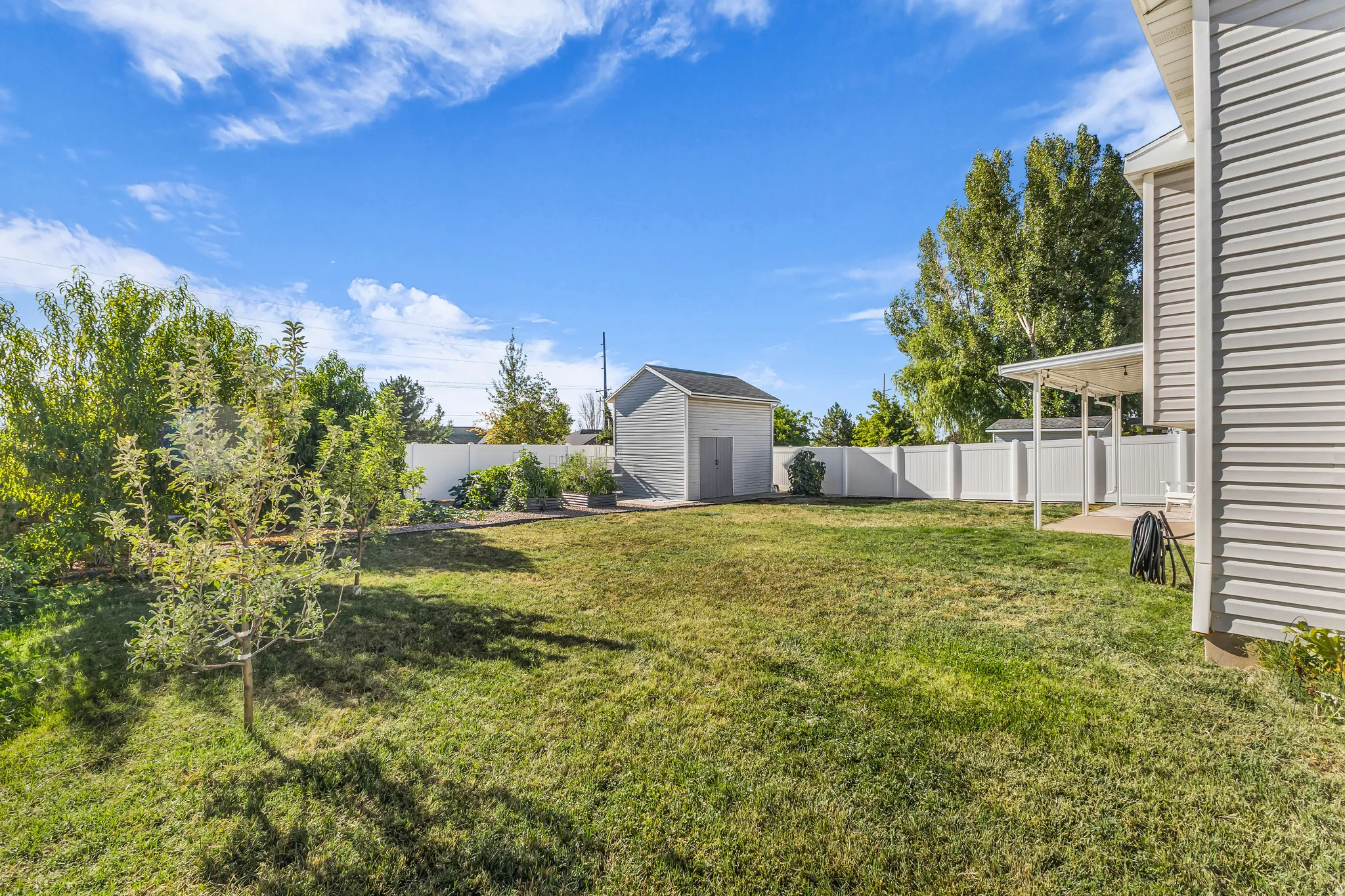 Fenced backyard featuring a storage shed, established trees, and a covered patio area