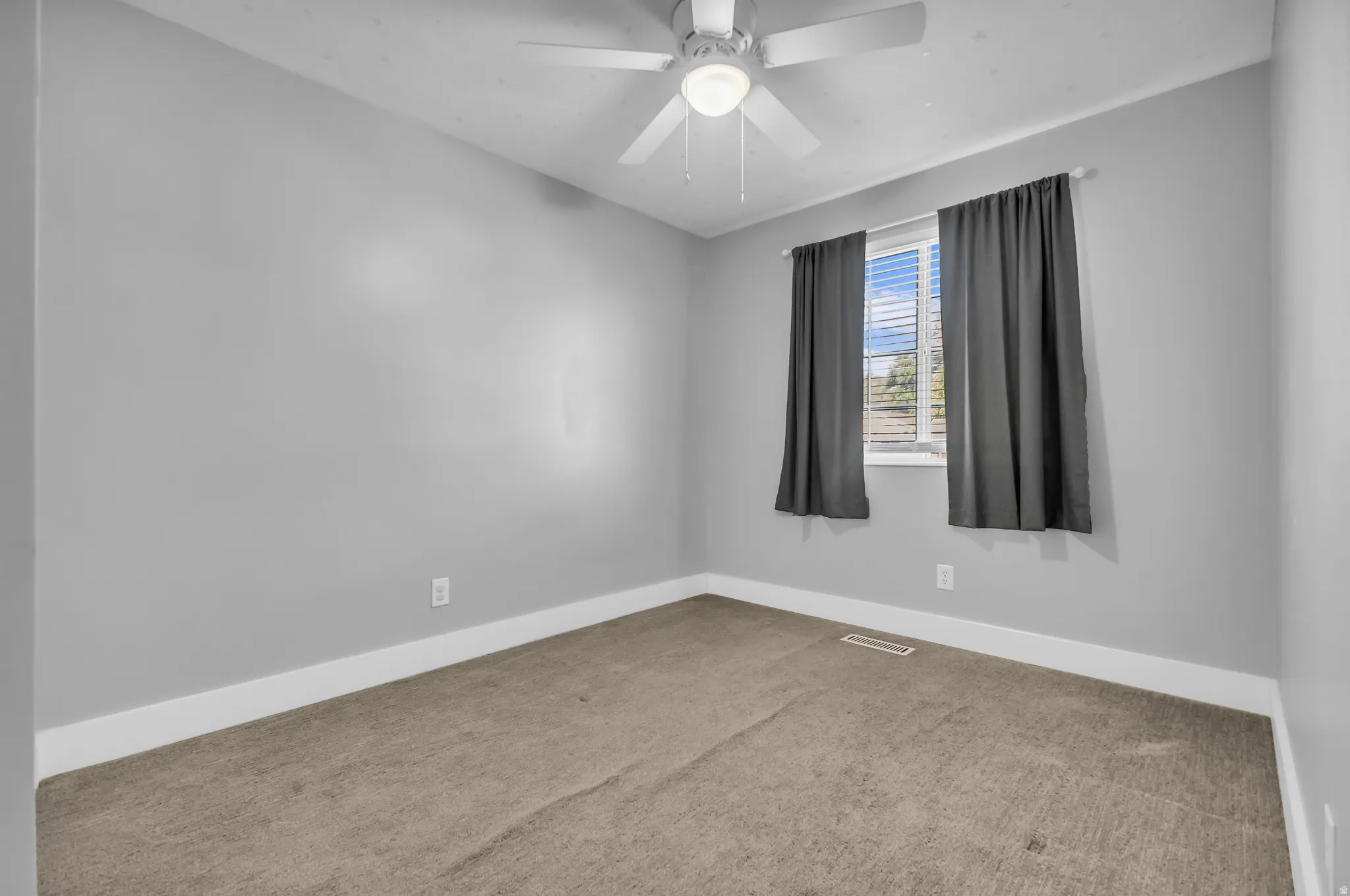 Carpeted flooring, light gray wall paint, white trim, window with blinds, and a ceiling fan with integrated lighting