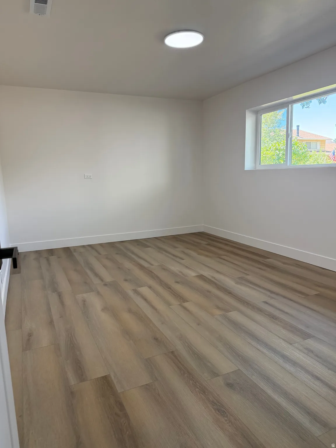 Wood-finish flooring with white baseboards, a single window, and a flush-mount ceiling light fixture