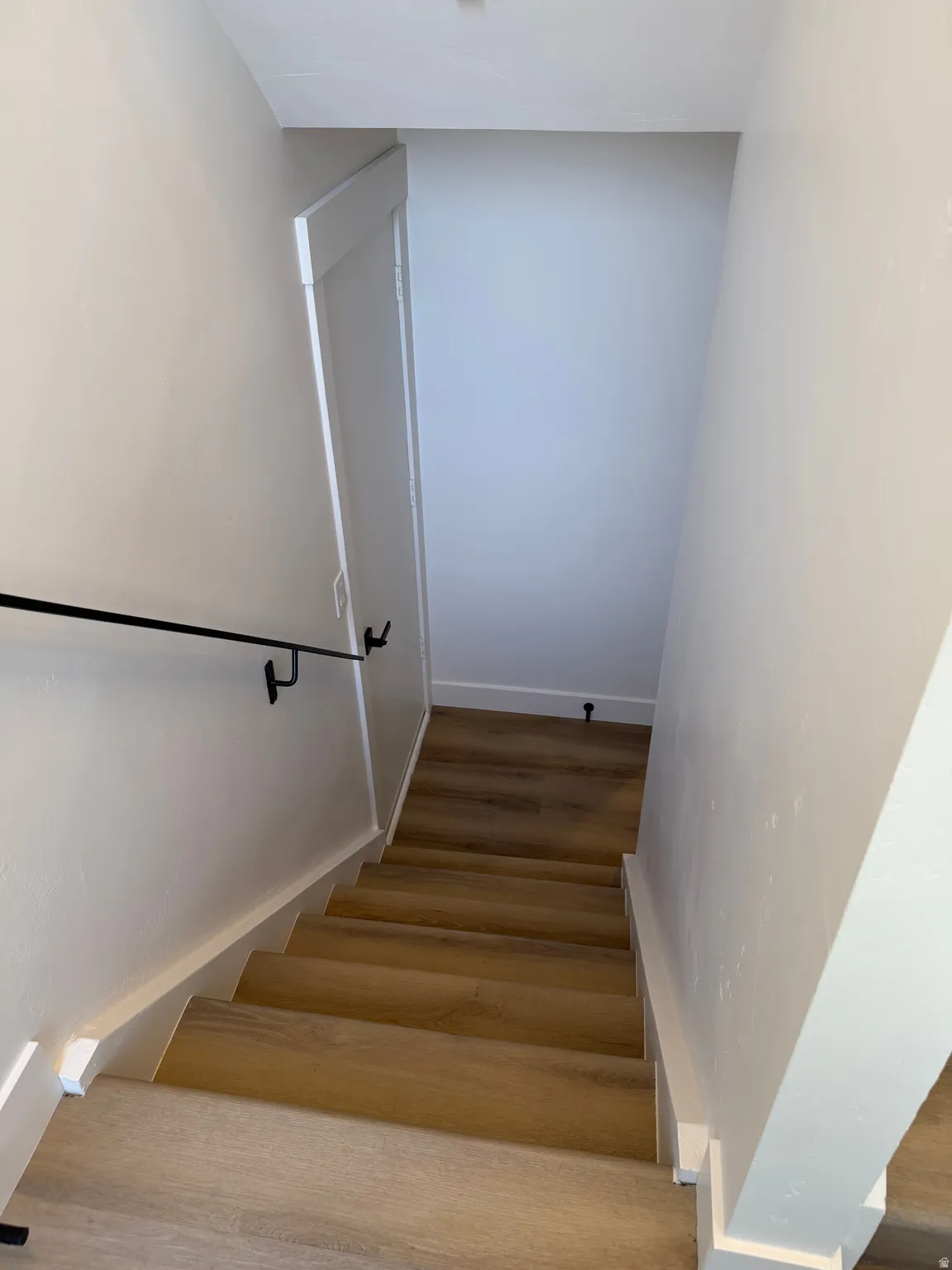 Staircase with wood-finish flooring, white risers, and a matte black handrail