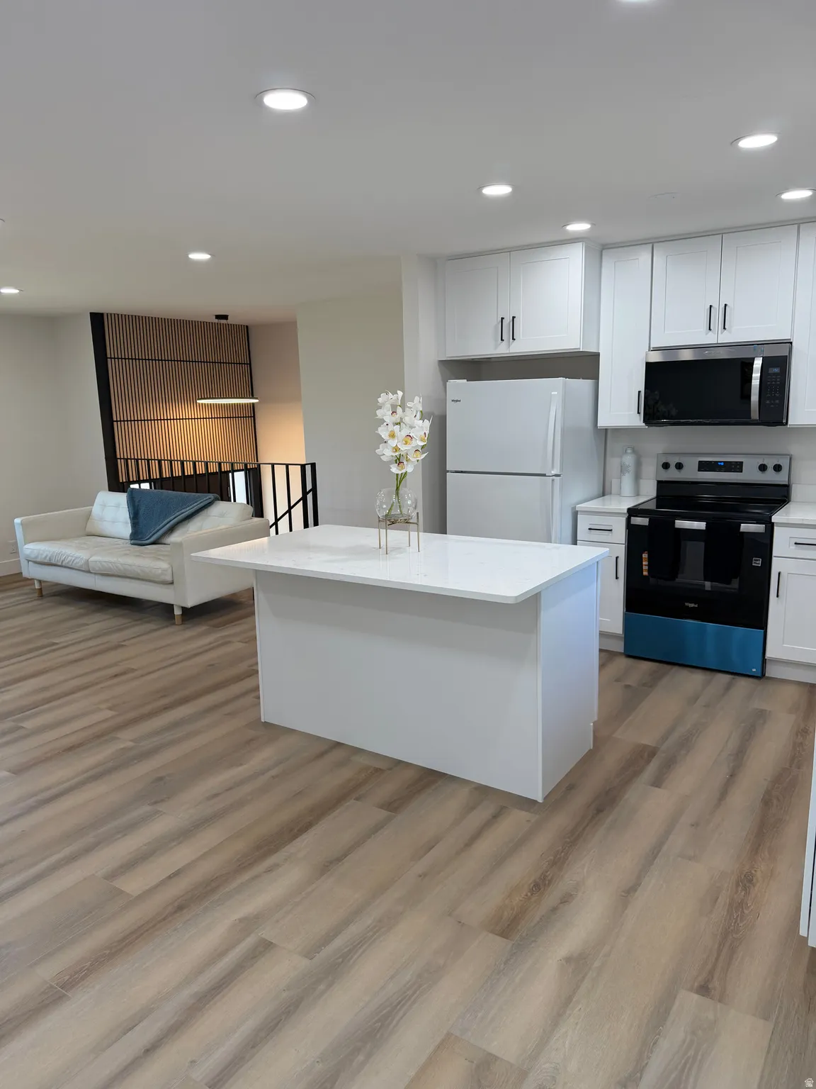 Modern kitchen featuring white cabinetry, a central island with a solid surface countertop, stainless steel appliances, and wood-finish flooring