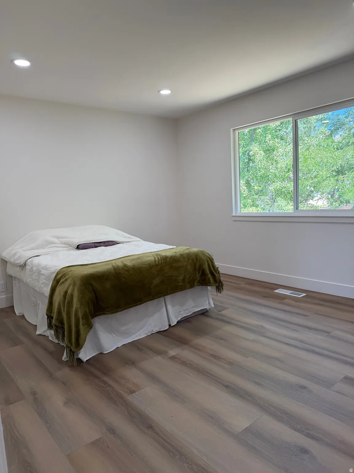 Recessed lighting illuminates the room, featuring wood-finish flooring and a large window with white trim