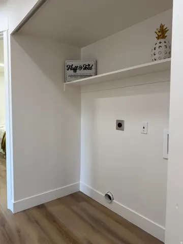 Laundry area featuring wood-finish flooring, white walls, and built-in shelving