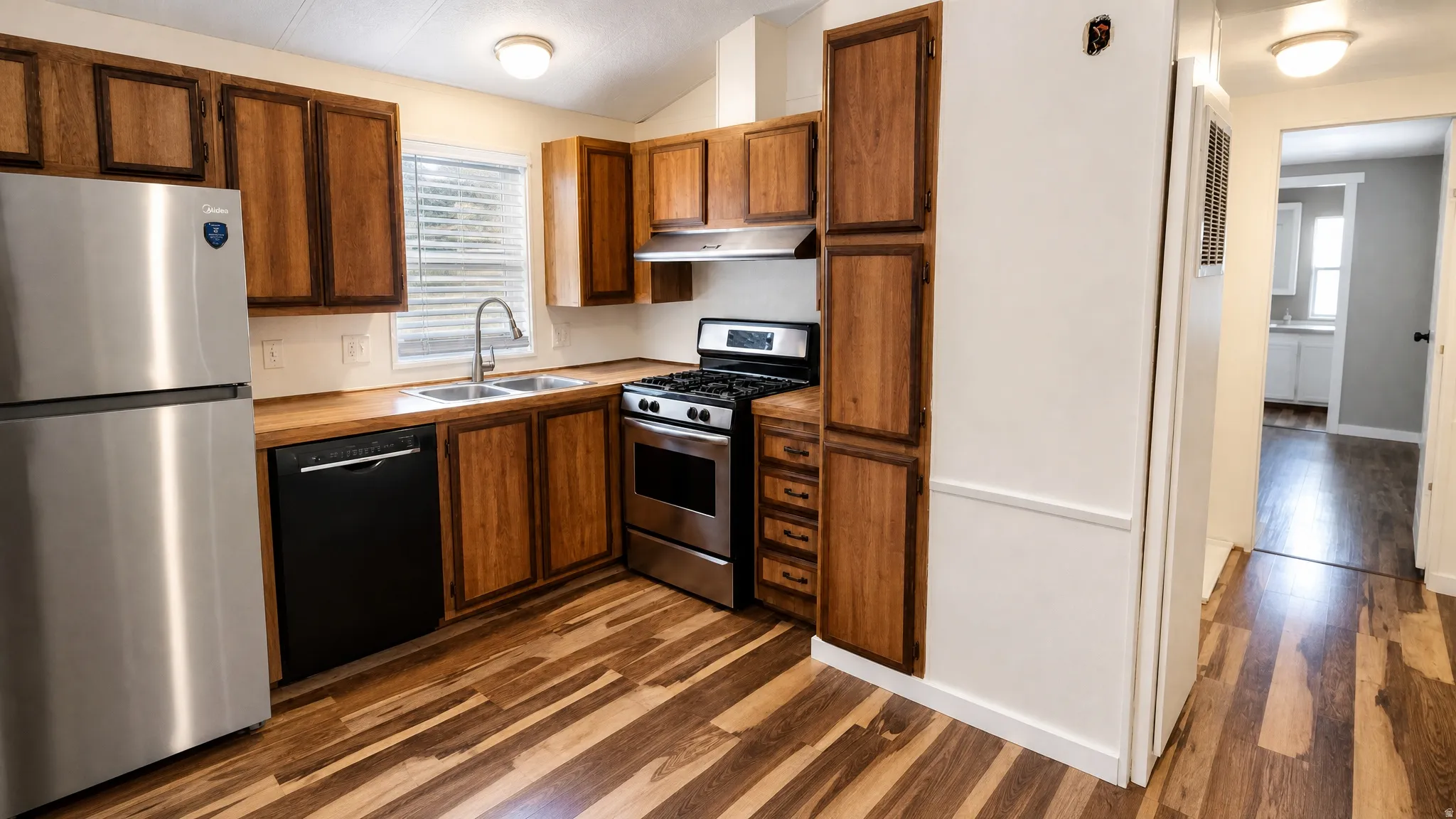 Kitchen featuring wood-finish flooring, stainless steel appliances, wood cabinetry, and a double basin sink