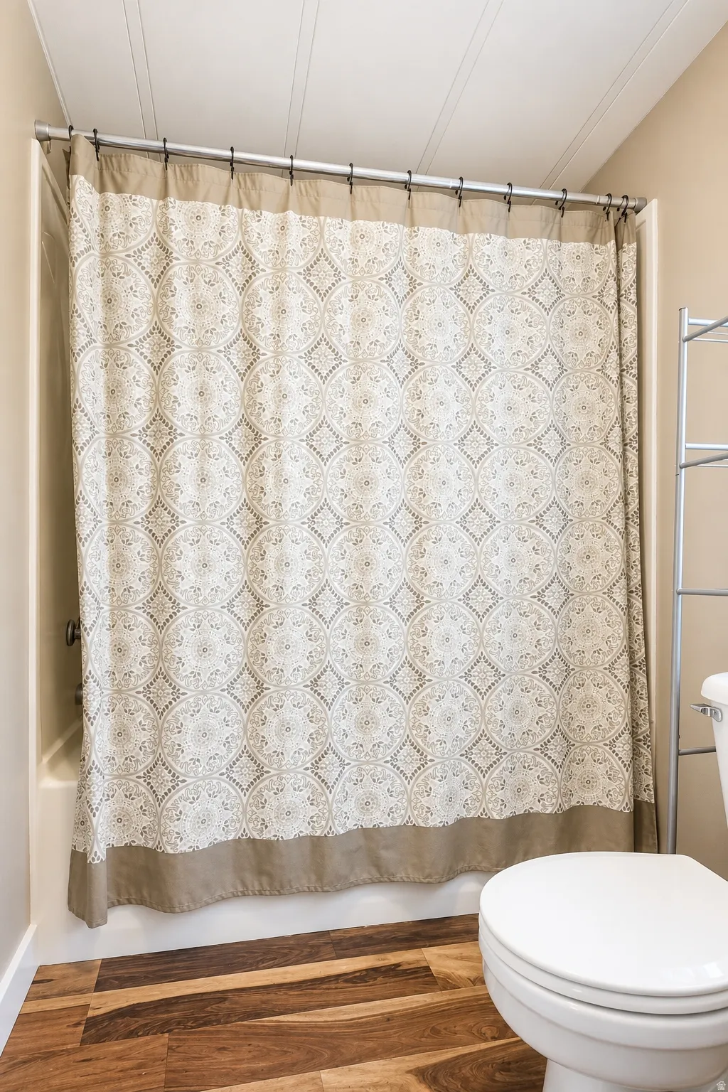 Primary Bathtub with a shower curtain, white toilet, and wood-finish flooring