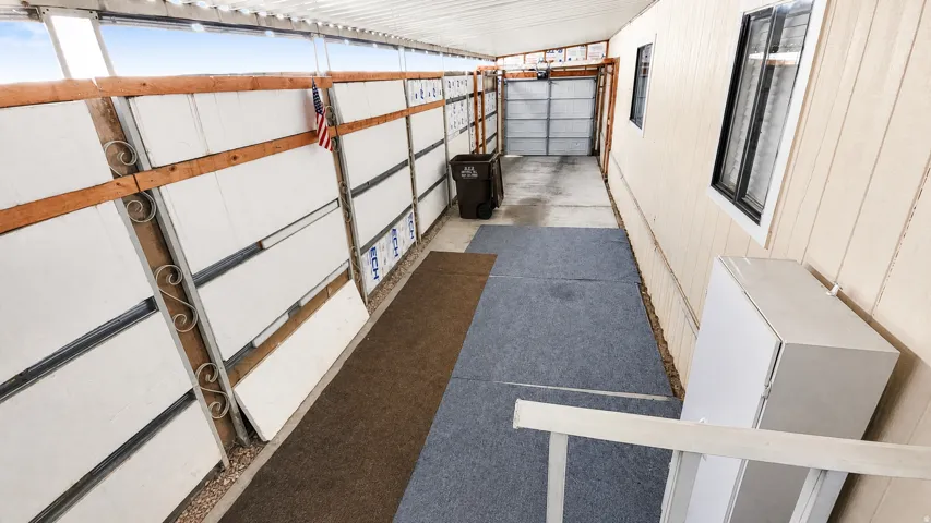 Covered walkway with a corrugated metal roof, wood-framed wall, and an attached 2 car tandem garage with a roll-up door