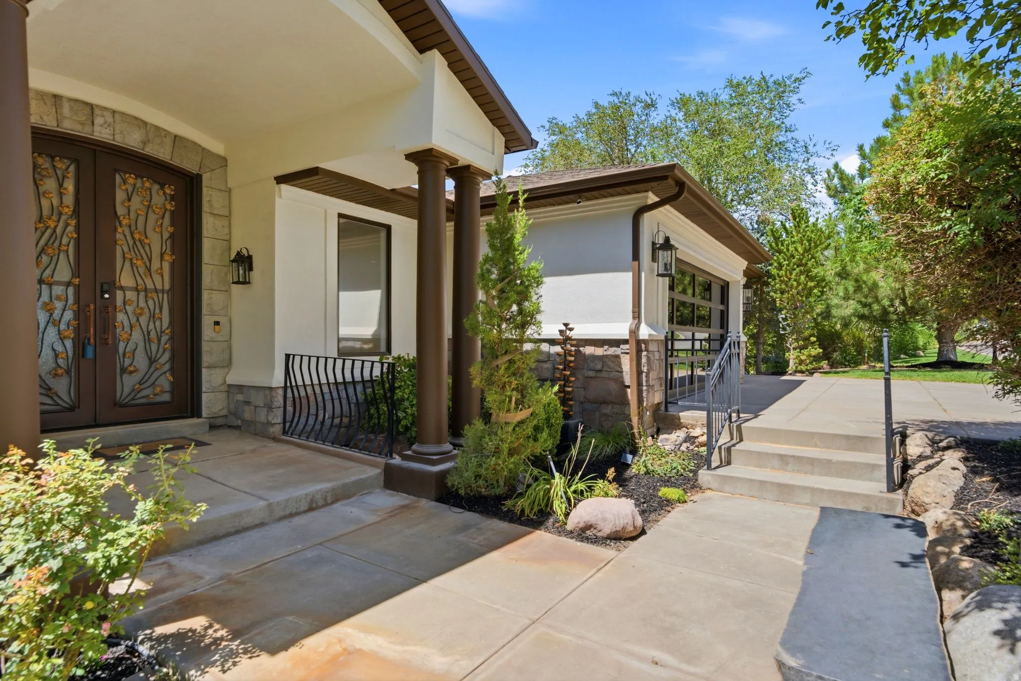 Stucco exterior with stone accents, covered entry with dark wood columns, ornate double entry doors, and an attached garage with a glass-paneled door